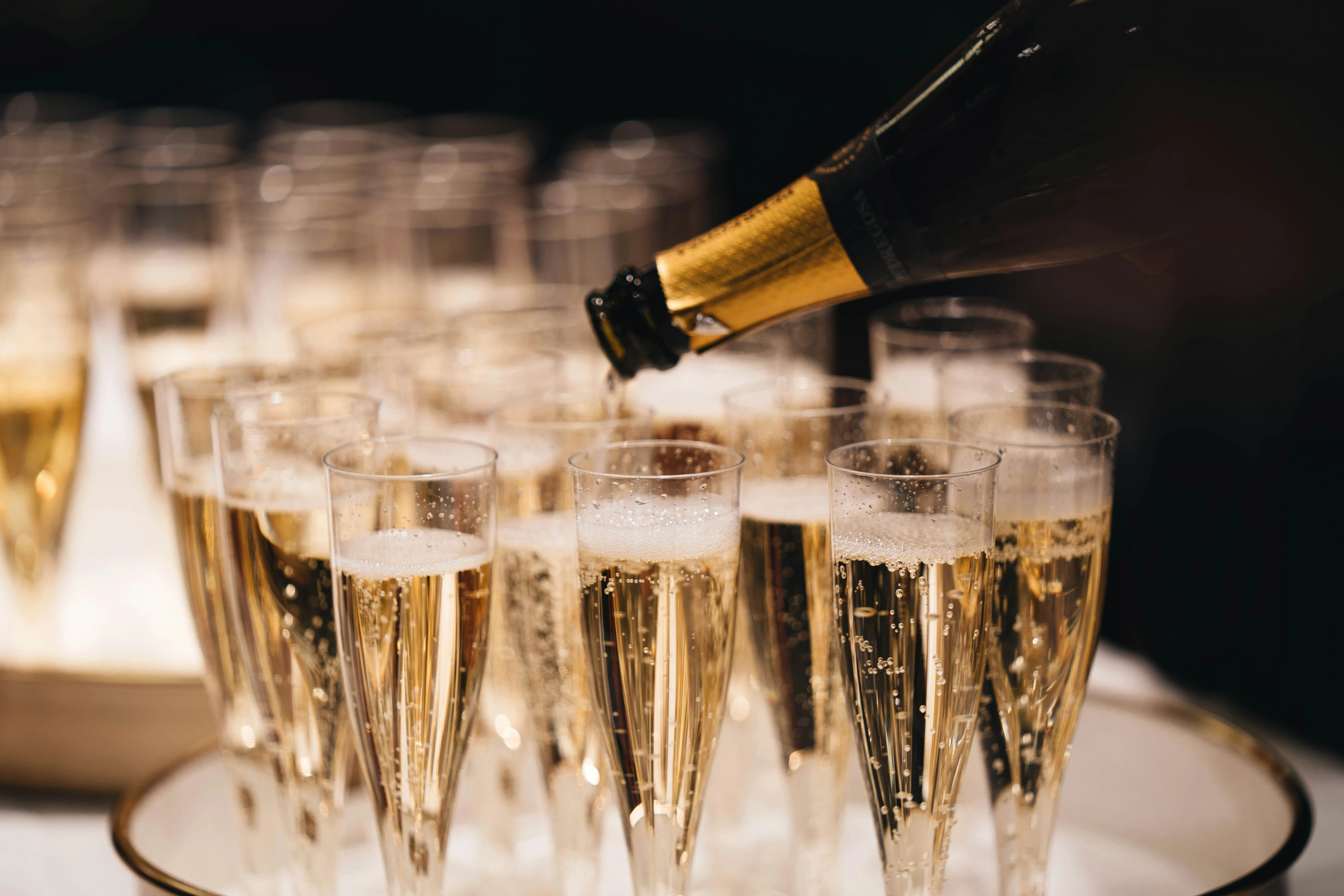 Sekt wird in viele schlanke Gläser eingeschenkt, bereit für einen feierlichen Empfang.